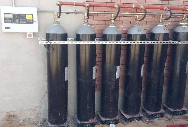 ست أسطوانات CO2 على حامل معدني موصولة بمجمّع أحمر، وإلى جانبها لوحة التحكم مثبتة على الحائط.