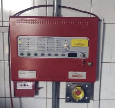 لوحة تحكم في الإطفاء بالغاز مثبتة على الحائط، وتحتها نقطة نداء يدوية (manual call point) وزر ضغط أصفر.