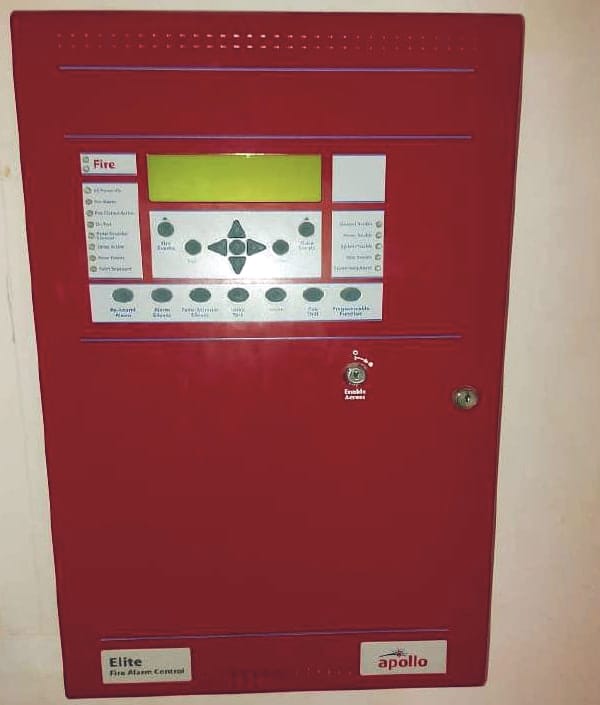 لوحة إنذار حريق حمراء بشاشة عرض (LCD) وأزرار تحكم ومفتاح تمكين، مثبتة على الحائط.